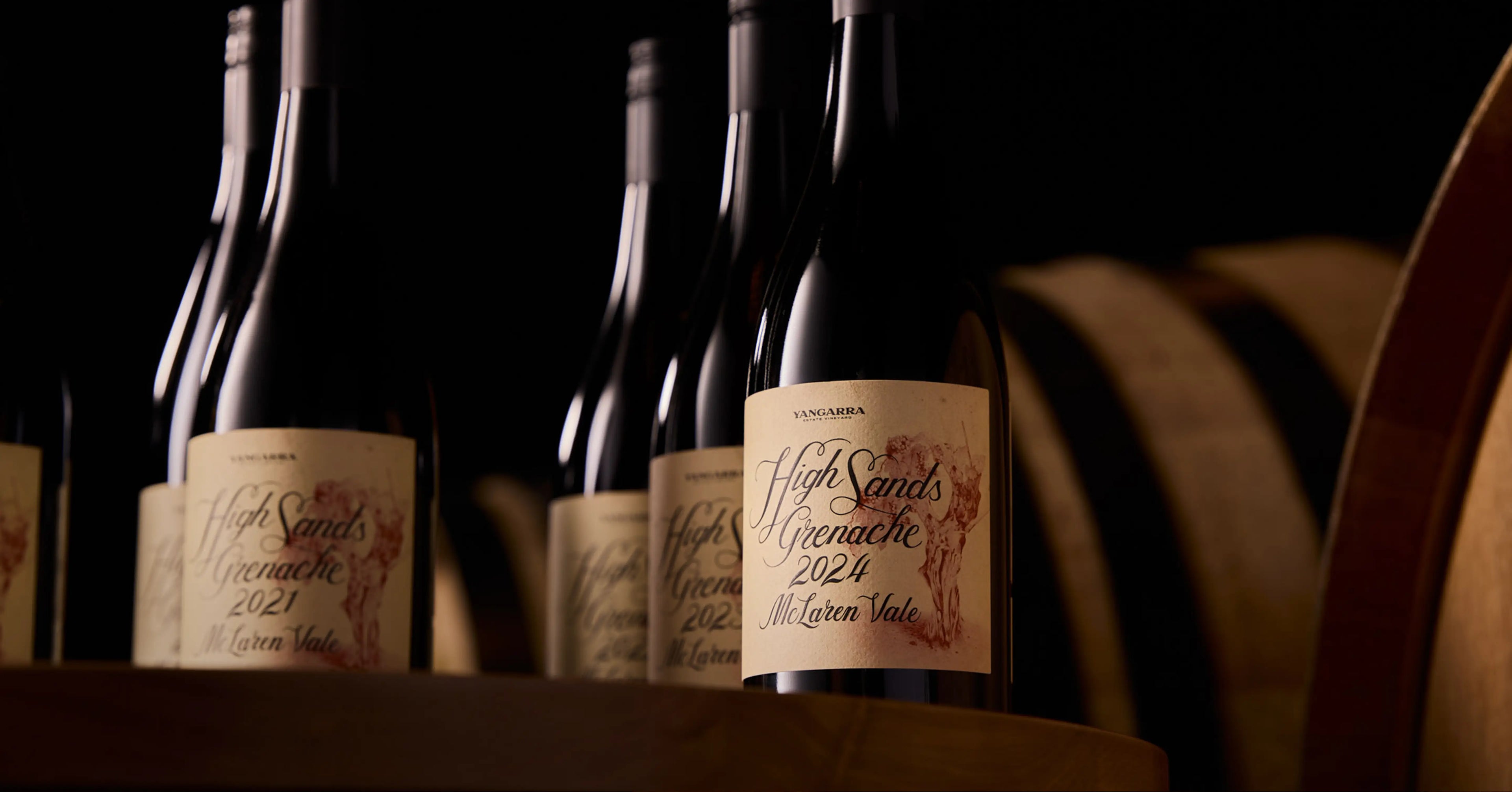 High Sands Grenache Wine bottles with labels in front of wooden barrels