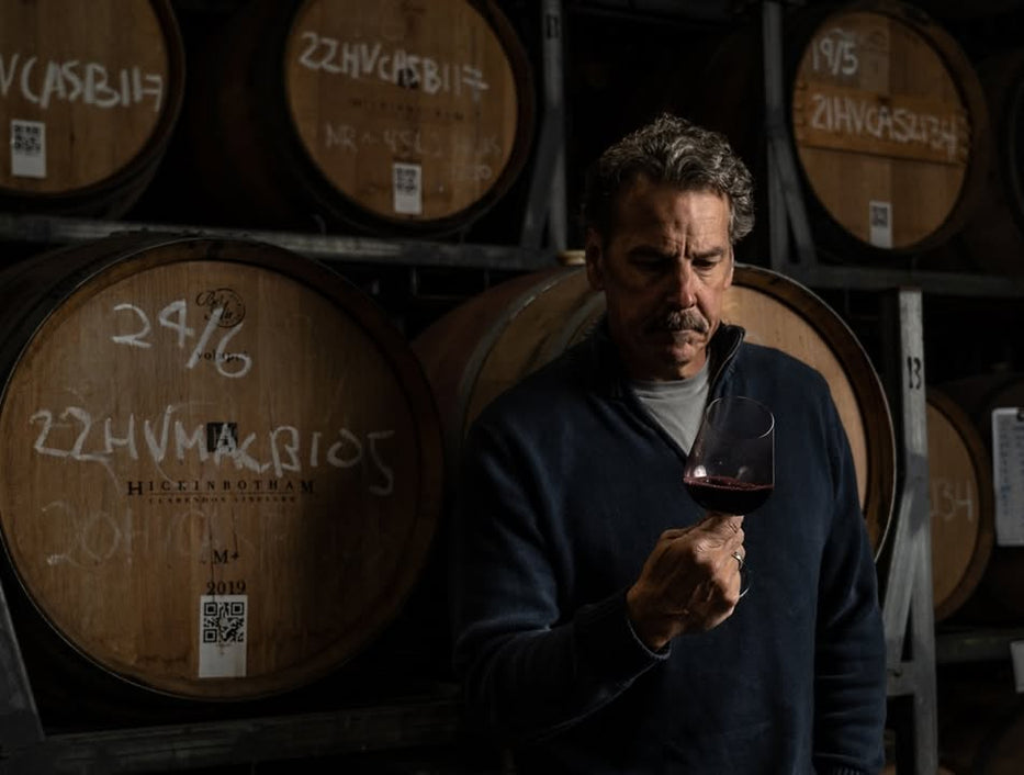 Man tasting wine in a winery with wooden barrels in the background