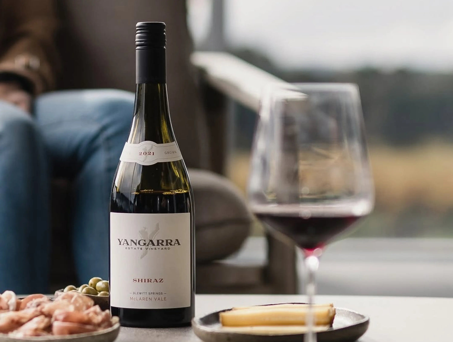 Bottle of Yangarra Shiraz wine with a glass on a table with snacks.