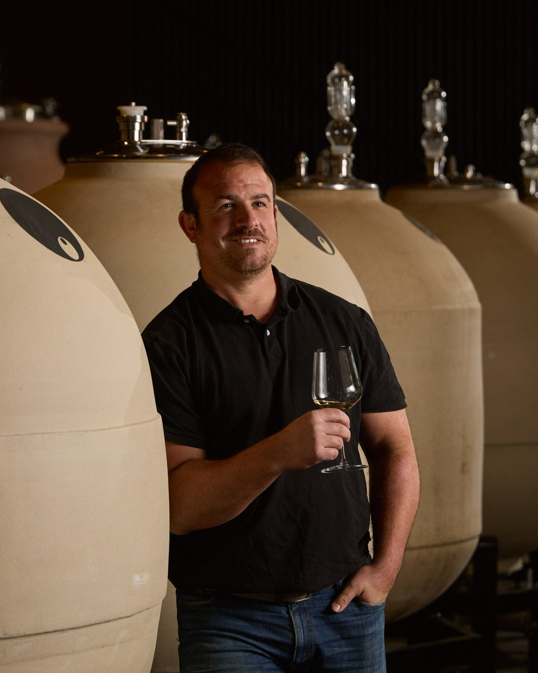 Guillaume Camougrand holding a wine glass in front of amphoras in winery.