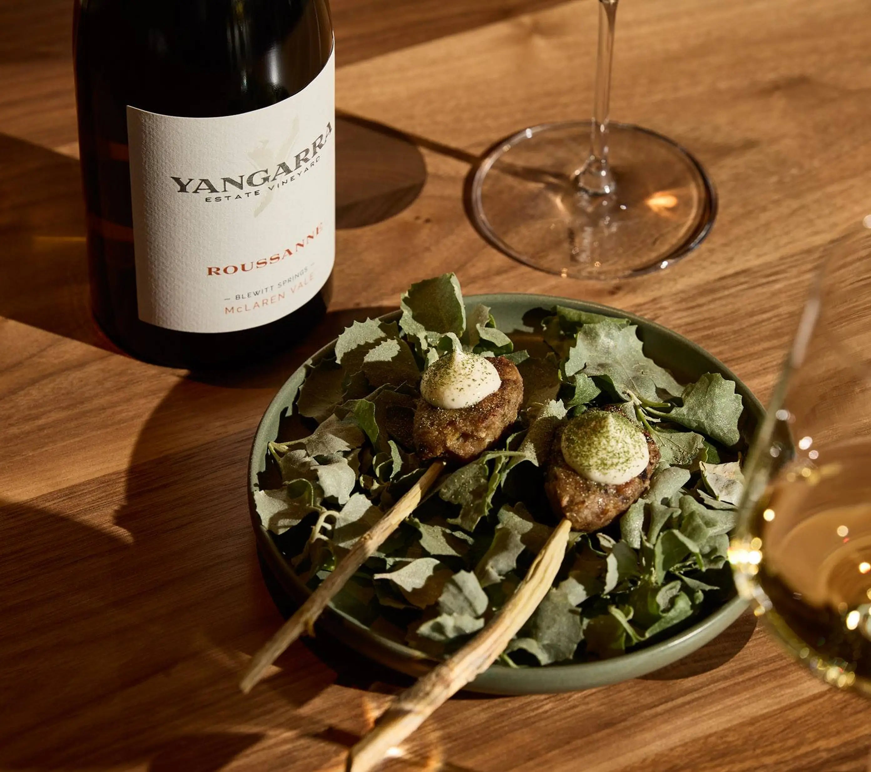 Bowl of appetizers with skewers on a wooden table next to a Yangarra bottle and glass of wine.